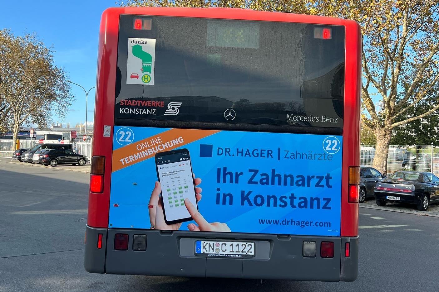 Buswerbung der von drhager auf der Rückseite eines roten Linienbusses im Straßenverkehr.
