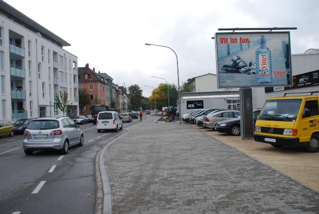City street with parked cars, a sidewalk, and a large billboard reading 'Vit is fun' overlooking a yellow van and buildings on a cloudy day, urban scene.