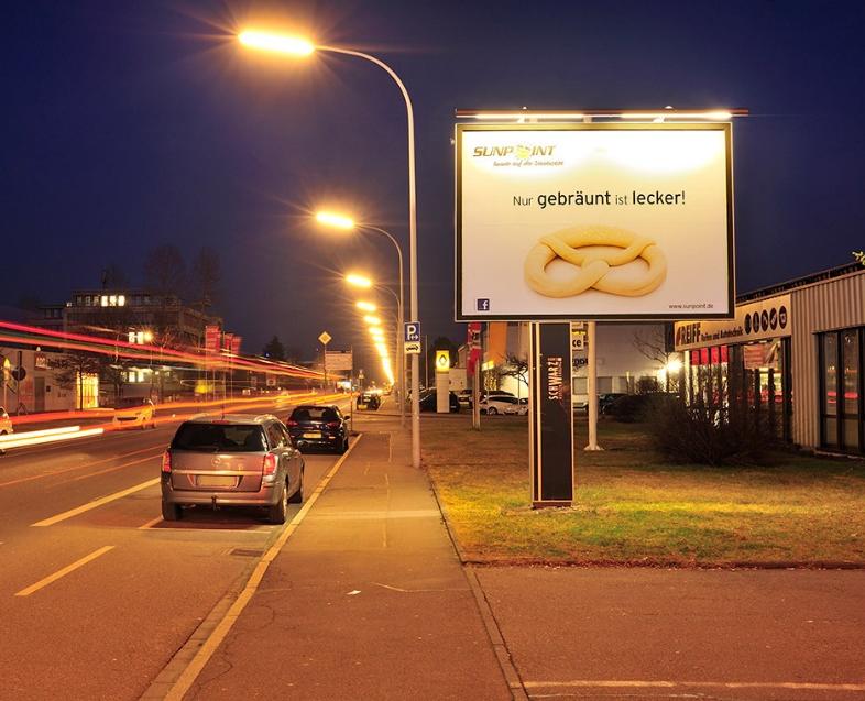 Monofuß-Werbeanlage auf Privatgrundstück an einer stark frequentierten Straße bei Nacht.