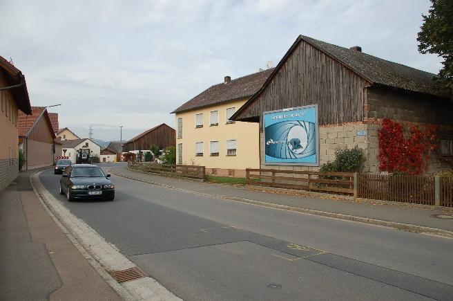 Großformatige Werbeanlage an einer Scheunenfassade entlang einer Ortsdurchfahrt.